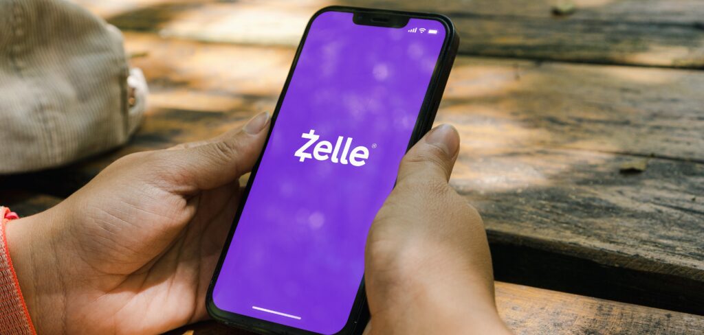 Girl in the park holding a smartphone with Zelle app on the screen.